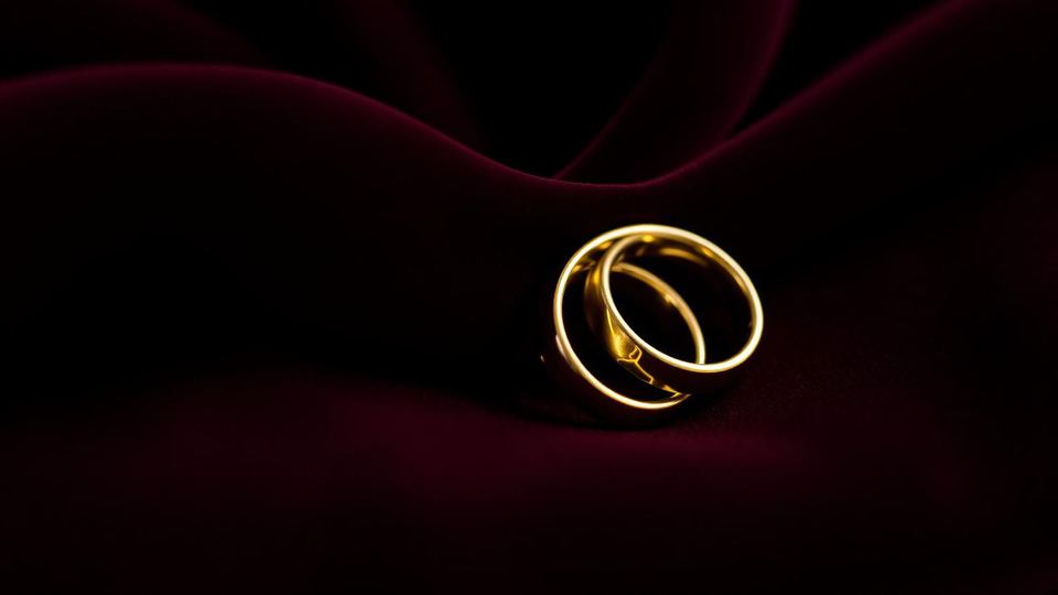 Two interlocking brass wedding rings resting on folded wine velvet